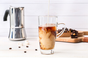 Pouring of milk into glass cup with tasty iced coffee on table