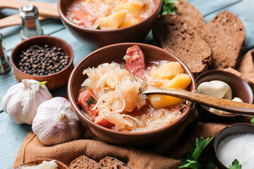 Bowls with tasty sauerkraut soup and ingredients on color wooden background