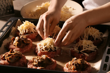 Woman adding grated cheese on minced meat boats with mushrooms, closeup