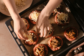 Woman adding grated cheese on minced meat boats with mushrooms, closeup