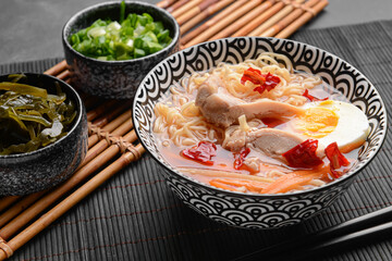 Tasty Chinese soup with chicken in bowl and seaweed on dark background