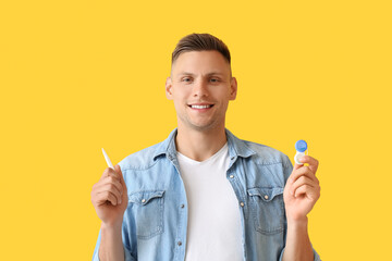 Young man with contact lenses and tweezers on color background