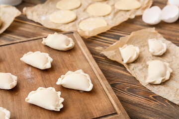 Fototapeta na wymiar Board with raw dumplings on wooden background, closeup