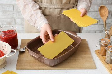 Woman preparing tasty lasagna at table in kitchen, closeup