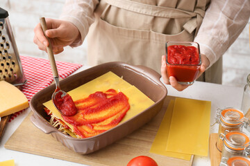 Woman preparing tasty tomato lasagna at table in kitchen, closeup