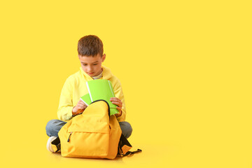 Little schoolboy with backpack and notebooks on color background