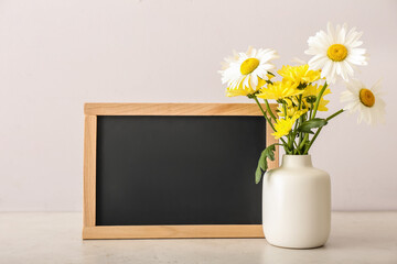 Vase with flowers and blackboard on light background. Teacher's Day celebration