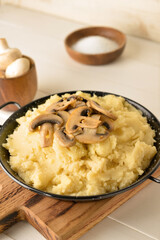 Frying pan with tasty mashed potatoes and mushrooms on light wooden background