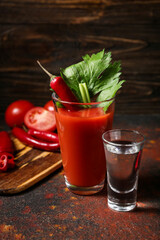 Glass of bloody mary cocktail garnished with cilantro, red chili pepper and vodka on table