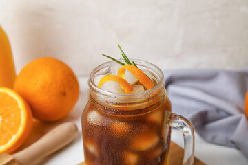 Mason jar of tasty coffee with orange juice on light background, closeup