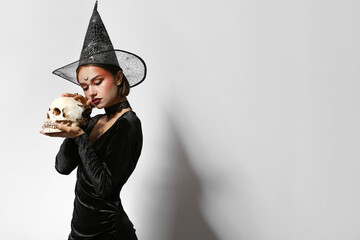 Young witch with skull and spider on light background