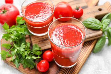 Glasses of tasty tomato juice on light background