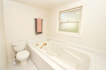 Interior room, bathroom with toilet next to large jacuzzi style bathtub. Tile walls and floor.