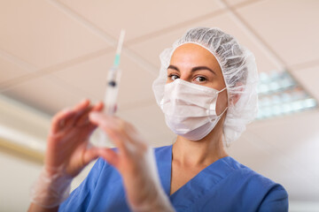 Female nurse in mask holding syringe for injection in hospital
