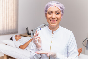 closeup on beautician holding microneedling smiling at a camera with the patient in the background