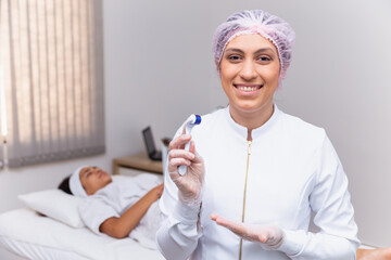 closeup on beautician holding microneedling smiling at a camera with the patient in the background