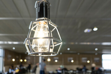 Close-up of a metal simple lamp with light bulb with blurry indoor in the background