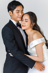 Young attractive Asian couple, soon to be bride and groom, woman wearing white wedding gown. Man wearing black tuxedo, hugging each other. Concept for pre wedding photography