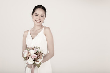 Portrait of young attractive Asian woman wearing white wedding dress smiling holding bouquet of flower in sepia. Concept for pre wedding photography