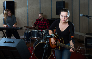 Fototapeta na wymiar Group of young musicians with passionate emotional woman vocalist and guitarist rehearsing in recording music studio