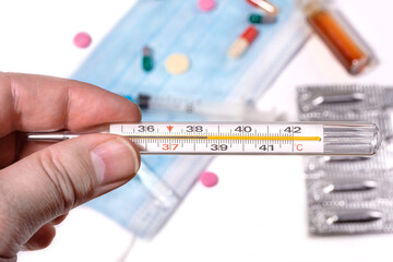 The hand holds a thermometer with a high temperature indicator against the background of a mask and...