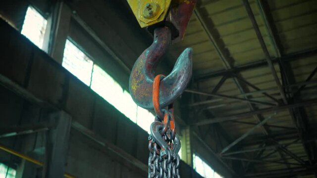 A hoist with a huge hook lifts the chains up. Factory or production in the background