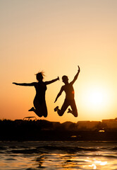 Fototapeta na wymiar Happy friends are having fun and jump at sunset beach in sunlight