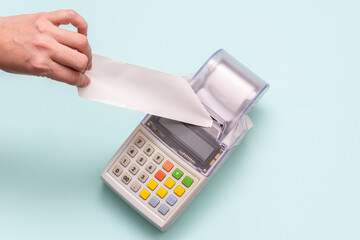 Close-up of a hand holding a blank white check on a cash register against a blue background, receipt, retail. Business concept, retail, online sale. Black Friday concept