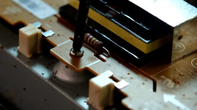An appliance repairman is unscrewing a nut from an electronic circuit board.