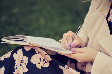 girl with pen writing on notebook on grass outside.