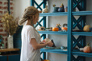 hostess of the ceramic workshop lays out her ceramic dishes on the shelves. feng shui concept. Small business office
