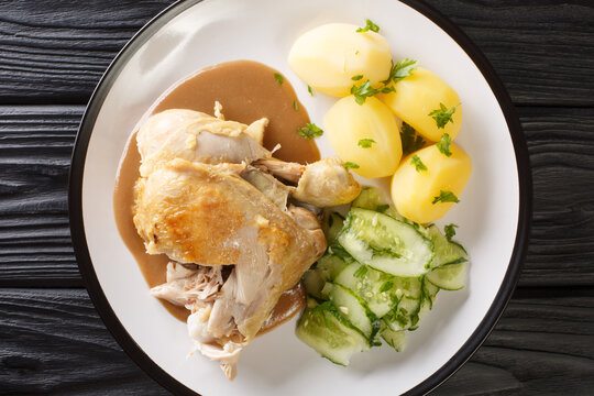 Danish fried old-fashioned chicken with boiled potatoes and cucumber salad close-up in a plate on the table. horizontal top view from above