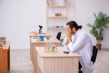 Young male chemist sitting at the desk in the classroom