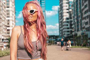 Young beautiful smiling hipster woman in trendy summer jeans shorts with pink hairstyle. Sexy carefree model posing in the street. Positive model outdoors in sunglasses