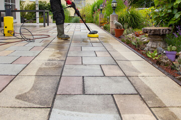 Cleaning stone slabs on patio with the high-pressure cleaner. Person worker in rubber boots...