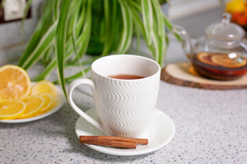 A hot tea drink with lemon and orange, a teapot and a white cup, served with delicious lemon and cinnamon. Fragrant and warming tea