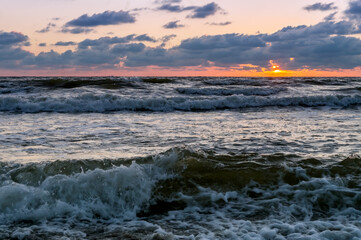 Fototapeta premium Sunset over the sea. Reflection of sunlight in the sea waves. Red and yellow sky in the rays of the sunset.