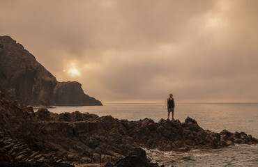 Fototapeta premium Man standing on rock looking at view of scenic beach during sunrise