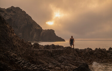 Man standing on rock looking at view of scenic beach during sunrise