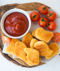 Homemade chicken nuggets with sauce and tomatoes on a wooden board