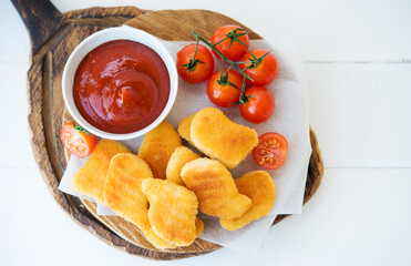 Homemade chicken nuggets with sauce and tomatoes on a wooden board, top view