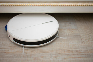 The robot vacuum cleaner cleans under the bed. Household help, new technologies, smart home, daily vacuuming. housework and technology concept, close-up