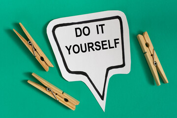 DO IT YOURSELF - word on white sticky note with wooden clothespins on green background