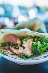 Close up shot of a Piadina sandwich, a typical italian flatbread, in a busy bar in Milan during aperitif hour. The piadina is filled with prosciutto ham, arugula and pink salsa.