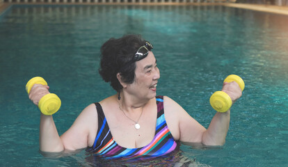 happy and healthy senior Asian woman  working out in the swimming pool with yellow dumbbells, smiling and looking away. Elderly sports , lifestyle. - obrazy, fototapety, plakaty