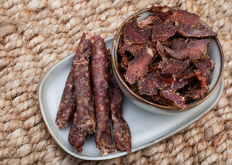 traditional South African Cured meat snacks, Biltong and dry wors. served in grey bowl on a rustic woven surface with copy space