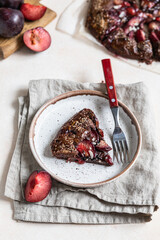Homemade galette or open pie with chocolate, plum and almond on light concrete background.