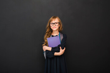 Girl kid 8-9 y.o. with black glasses and with a books looking at camera in isolation on a black background. Back to school.