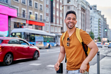 Young smiling Latino man walking through the streets of Madrid. Walking down main street of the city. 