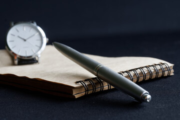 Metalized ballpoint pen and a spring-loaded notebook lie next to the wristwatch. Concept of will, notary, memoir and deadline. Selective focusing